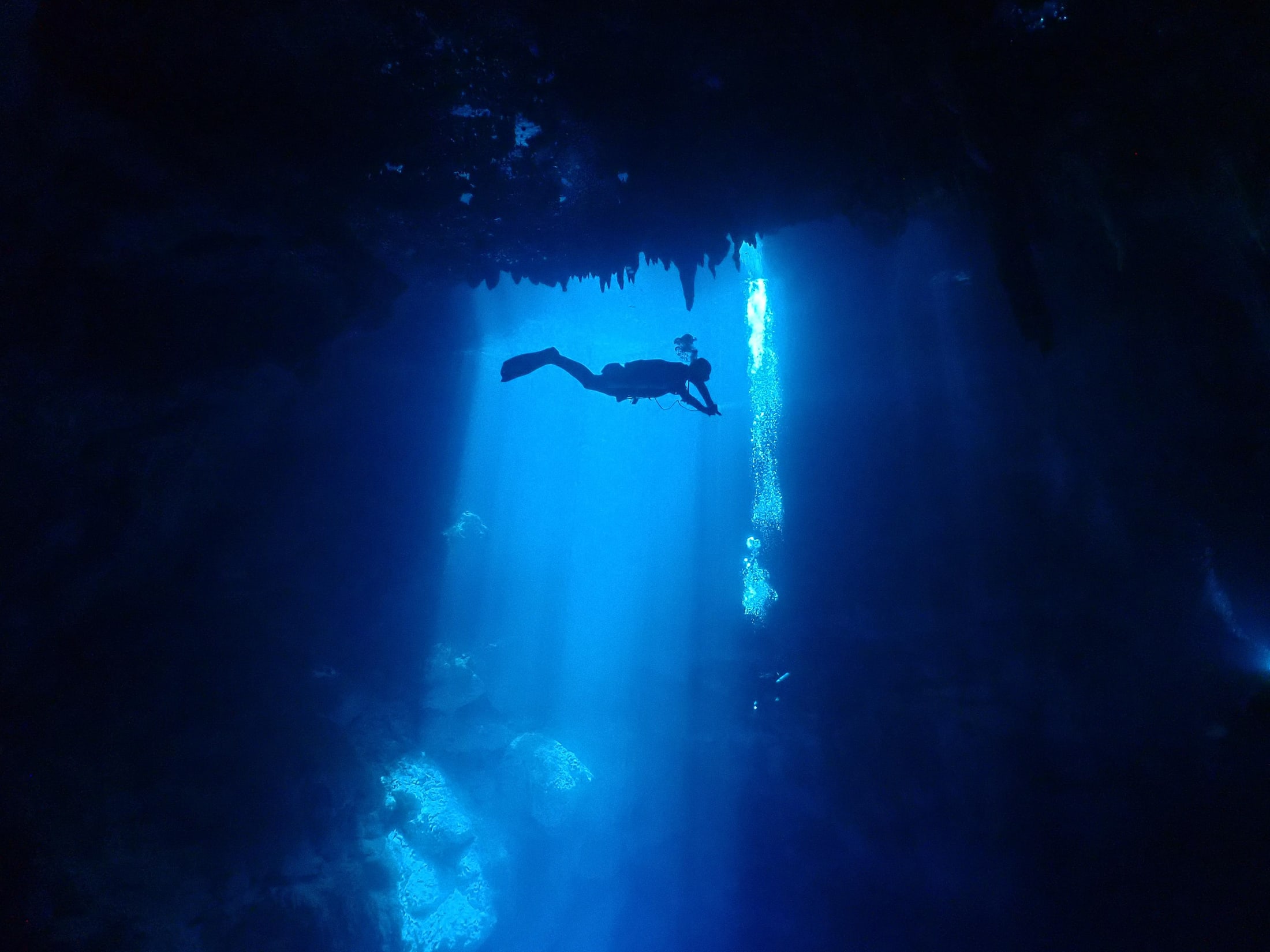 A scuba diver beneath a beam of light inside a cenote